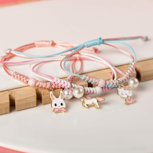 Bracelet tressé avec pendentif perle et animal rose et bleu sur fond blanc et bois