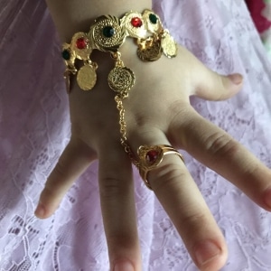 Bracelet et bague reliés par une chaîne pour petite fille sur une main d'enfant avec une jupe blanche