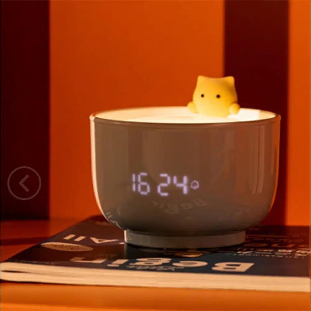 Veilleuse en forme de tasse de thé avec réveil avec chat dedant sur une magazine et un plan derriere orange