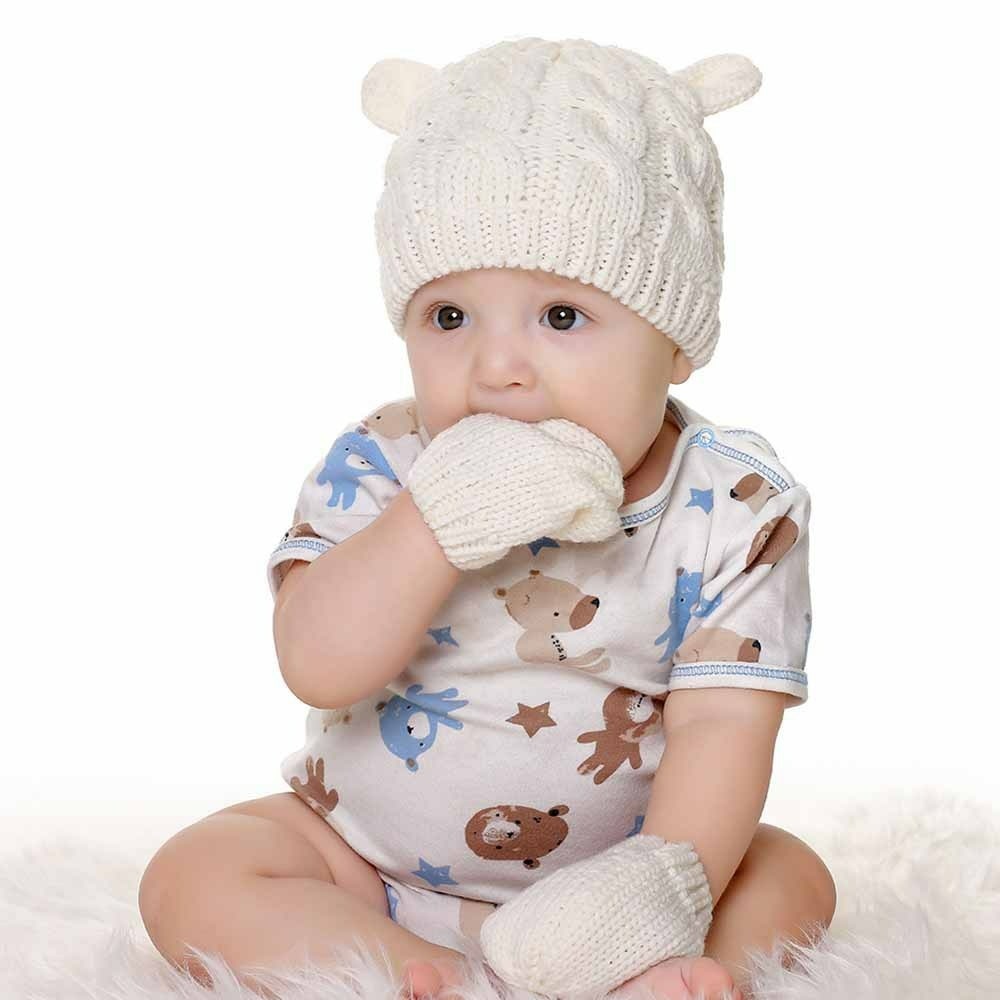 Ensemble bonnet et moufles d'hiver pour bébé blanches avec bebe avec sa main dans la bouche et vetement blanc avec motifs