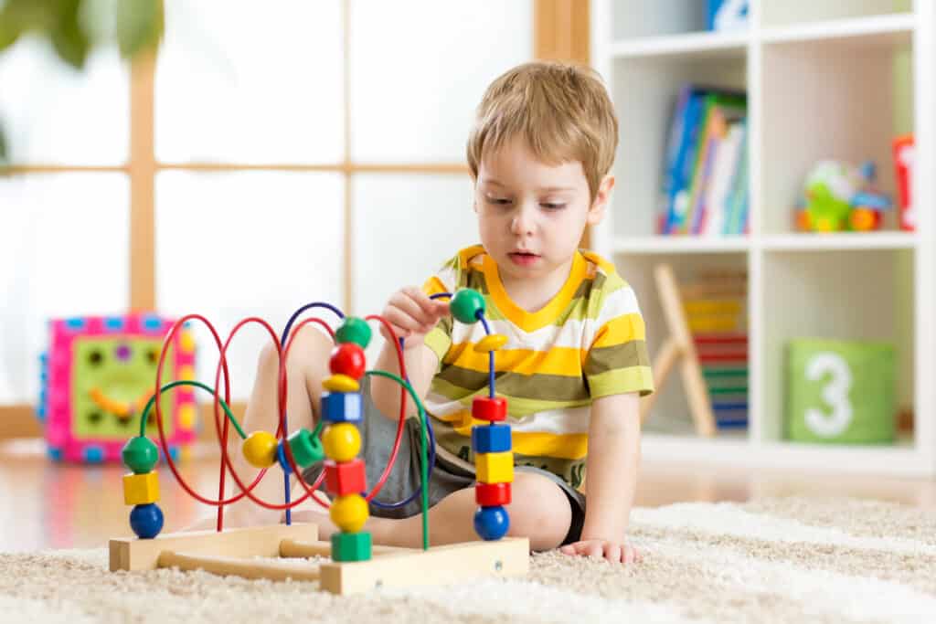un petit garçon joue avec un jeu éducatif assis dans une chambre remplie de jouet