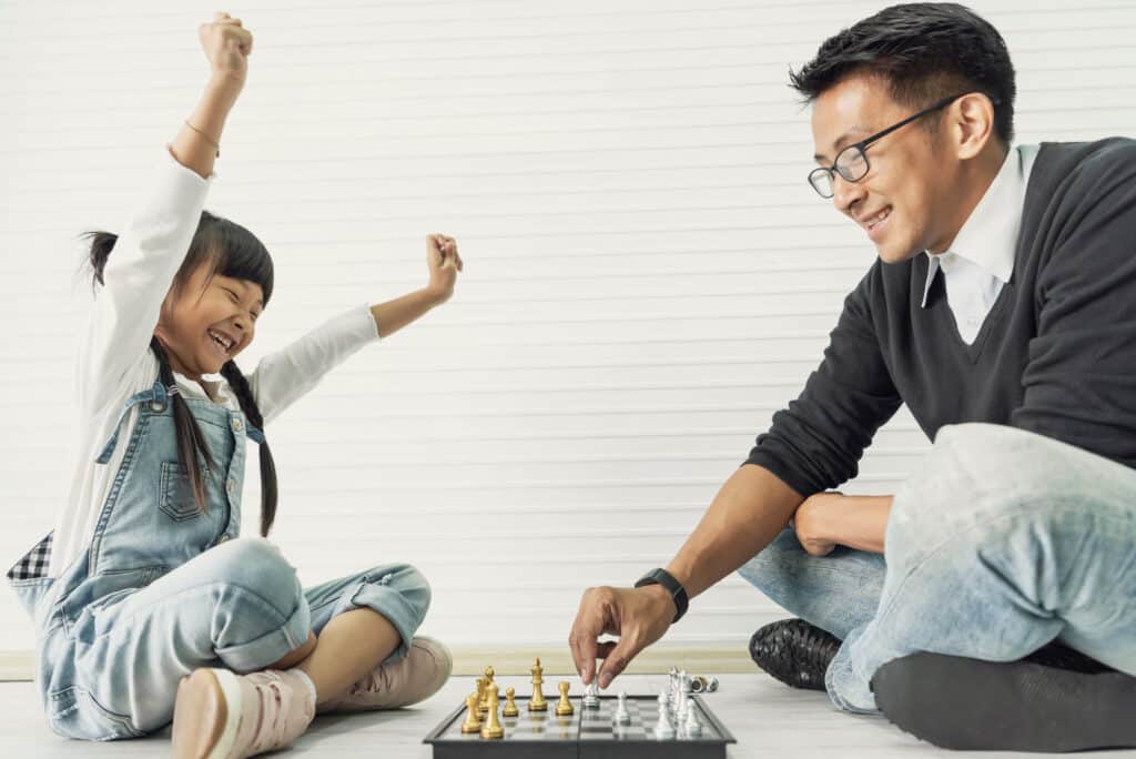 Une petite fille asiatique qui joue aux echecs avec son papa. le jeu d'echec est gris et doré