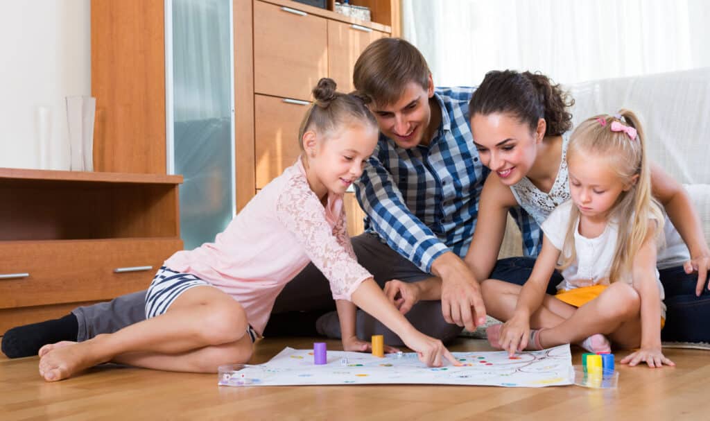 Une famille heureuse qui joue à un jeu de société assis par terre dans la chambre.