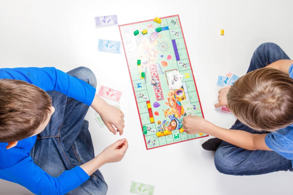 Deux jeunes enfants qui jouent au monopoly l'un a un pull bleu l'autre un t shirt bleu