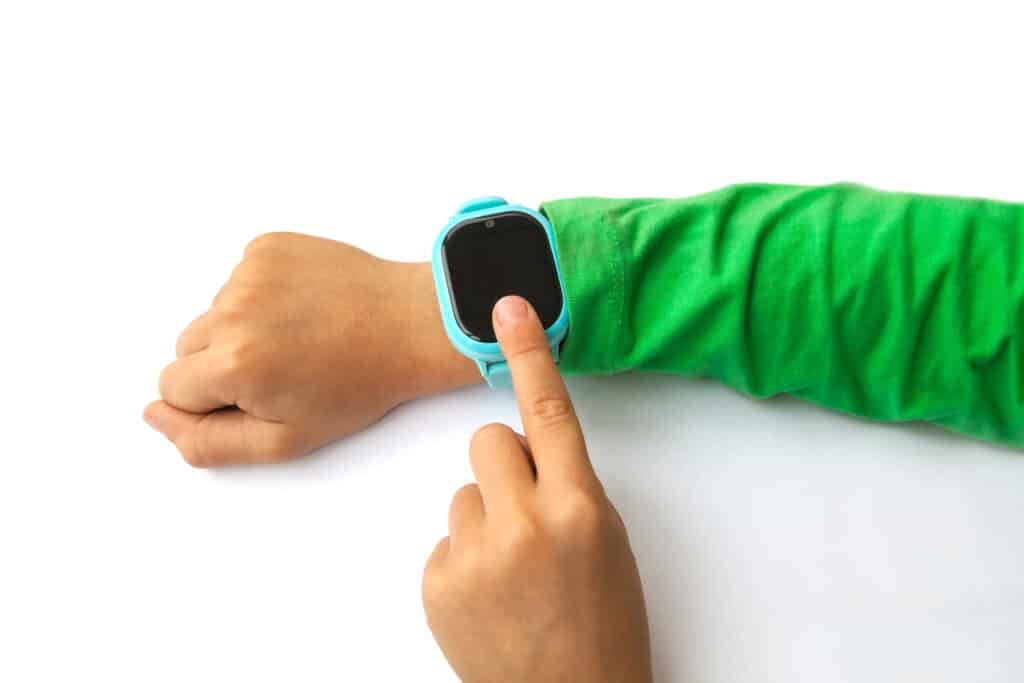 Un bras d'enfant qui porte une montre connectée pour enfant bleu avec une manche de gilet verte
