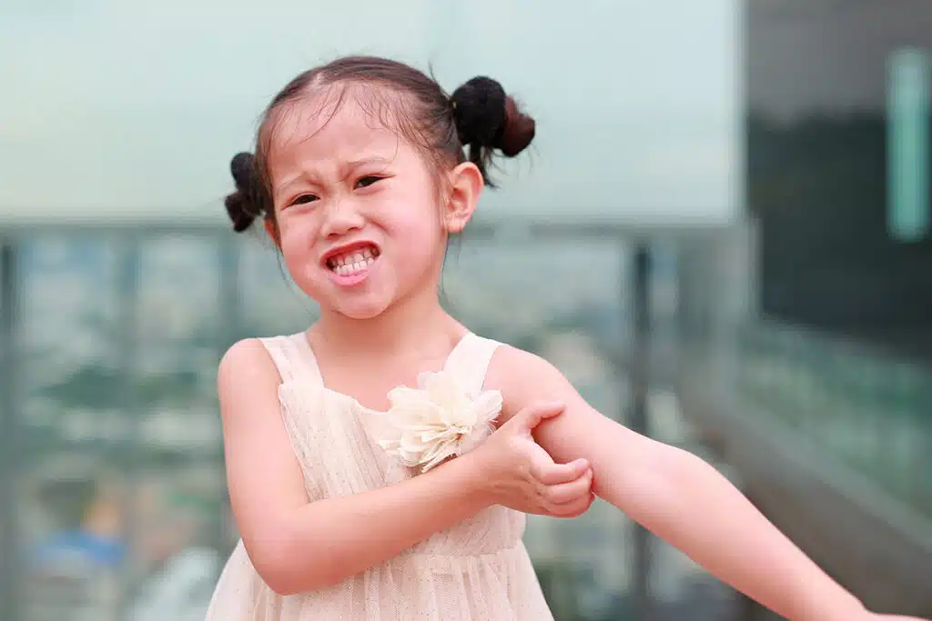 Une petite fille asiatique qui fait la grimace en se grattant à cause des allergies.
