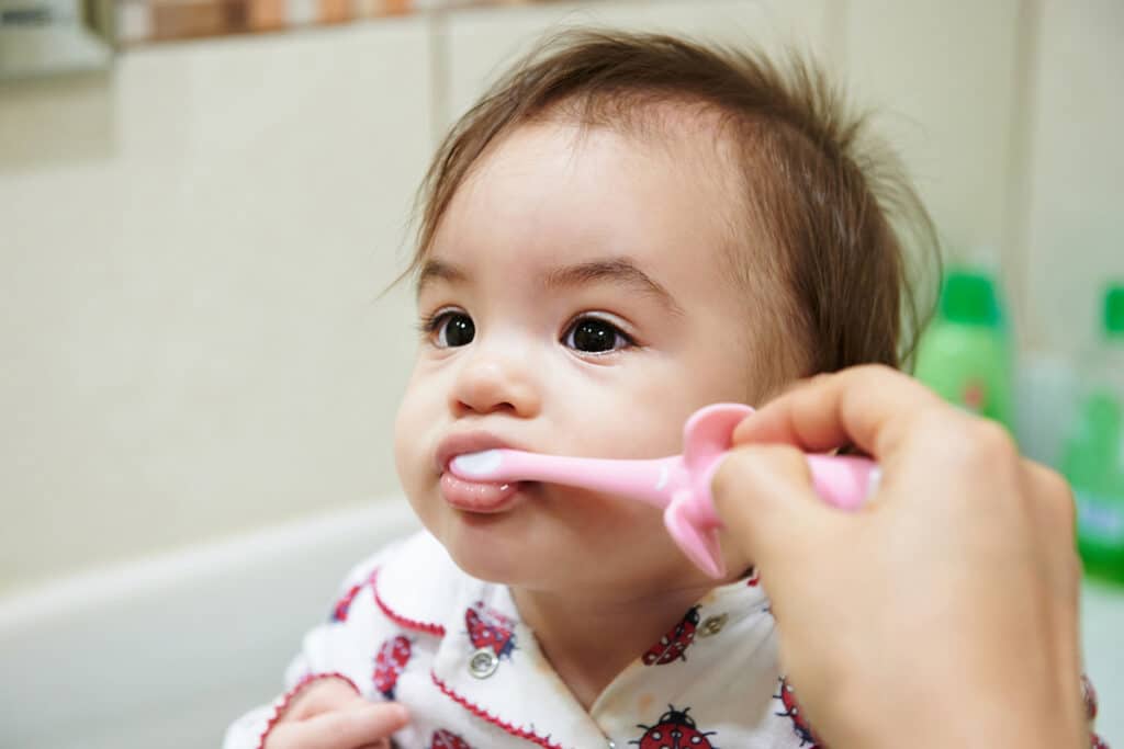 Un jeune bébé qui se lave les dents avec une brosse à dent rose. il est dans une salle de bain.