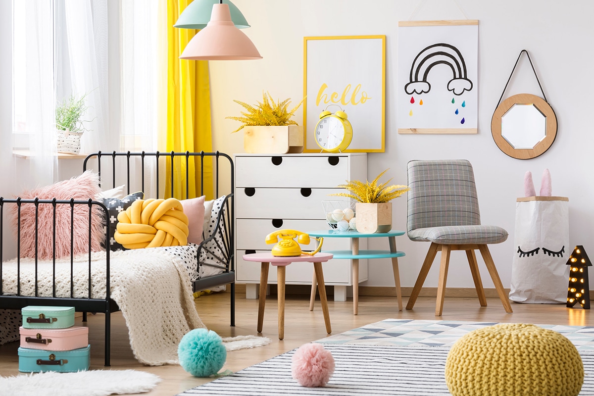 Pouf jaune, chaise grise et lit à barreaux à l'intérieur d'une chambre d'enfant colorée avec affiche et décorations au mur