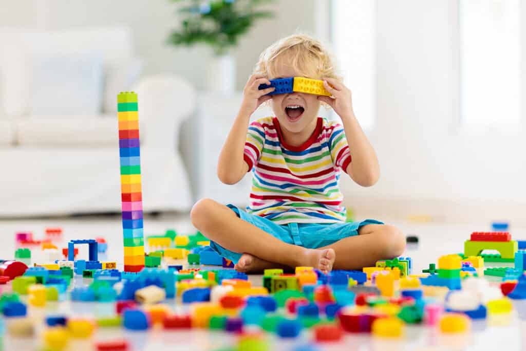 Jeune enfant blond jouant avec des blocs de jouets de construction colorés. le Petit garçon est assis par terre à la maison 