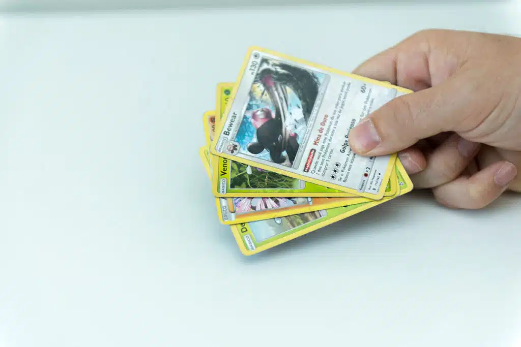 Une main qui tient 4 cartes pokemon sur fond blanc.