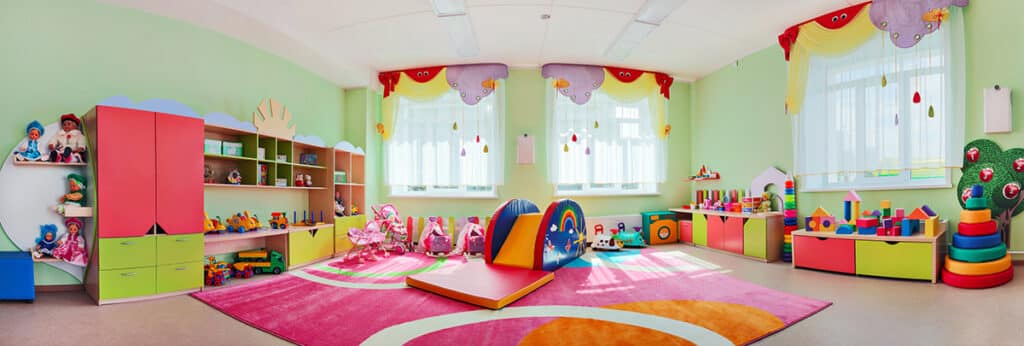 Vue panorama d'une grande salle de jeu pour enfant colorée. Il y a des meubles de rangement de couleurs, des tapis moelleux colorés, et tous un tas de jeux pour enfant.