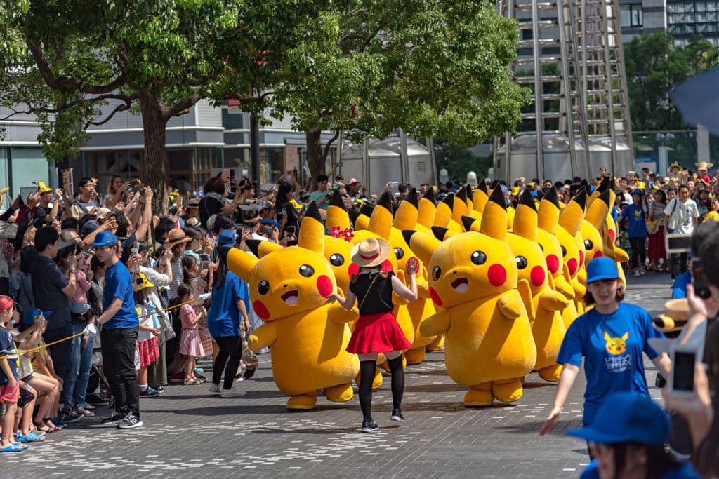 Un défilé d'une vingtaine de Pikachu grandeur nature. Ils défilent pour Pokémon à Yokohama. La foule est réunie autour des Pikachu.