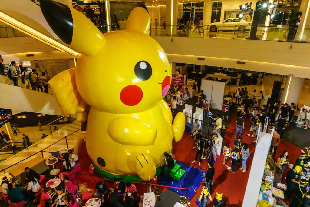 Un gros ballon en forme de Pikachu. Le ballon en forme de pokemon est posé dans un centre commercial aux milieux de la foule.