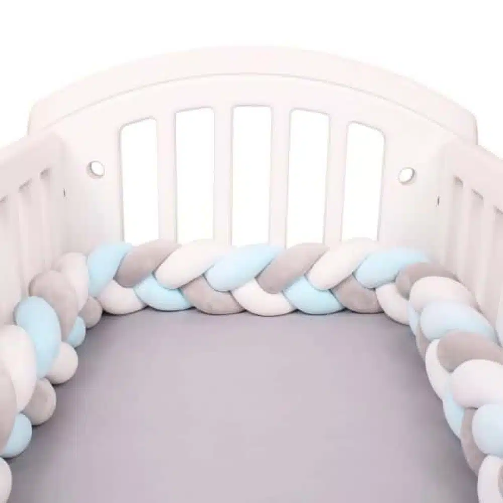 Tour de lit tressé blanc gris bleu dans un lit de bébé blanc avec draps en gris