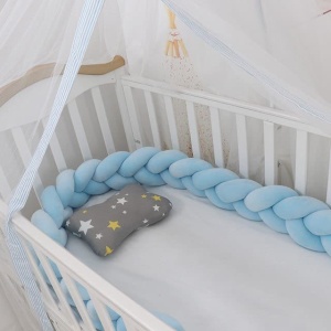 Tour de lit tressé bleu dans uin lit de bébé blanc avec draps en blanc et un rideau transparent