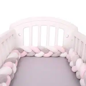 Tour de lit tressé rose blanc gris dans un lit de bébé blanc avec draps en gris