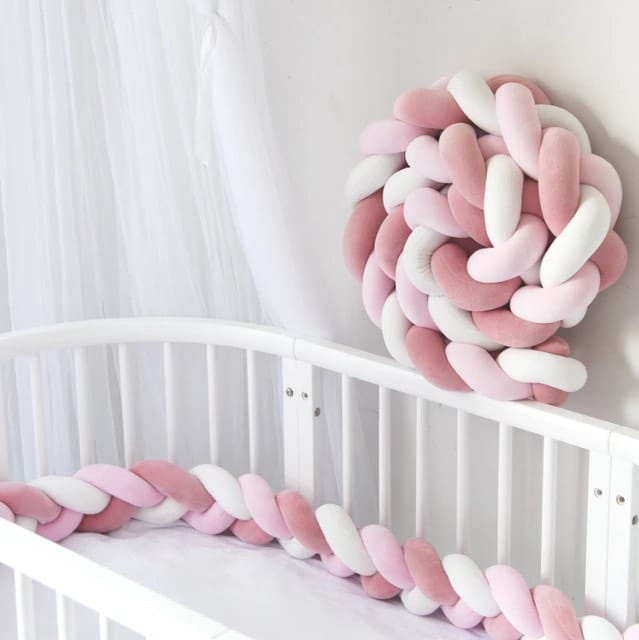 Tour de lit tressé rose et blanc sur un lit de bébé blanc et un mur blanc