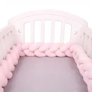 Tour de lit rose tresse dans un lit de bebe blanc avec draps gris