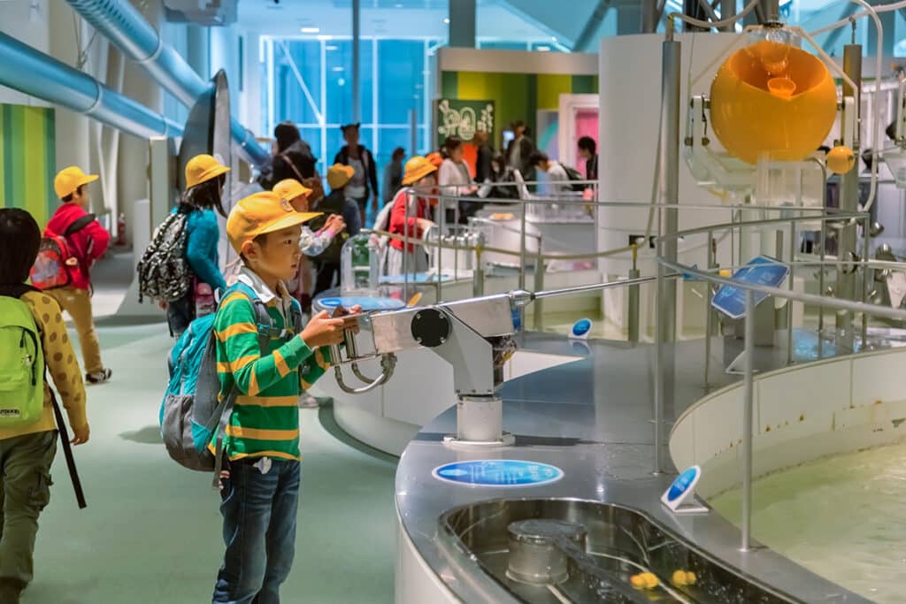 Un musée à Nagoya au japon. Il y a des enfants d'une classes qui observent l'intérieur du musée. Tous les enfants portent la même casquette jaune.