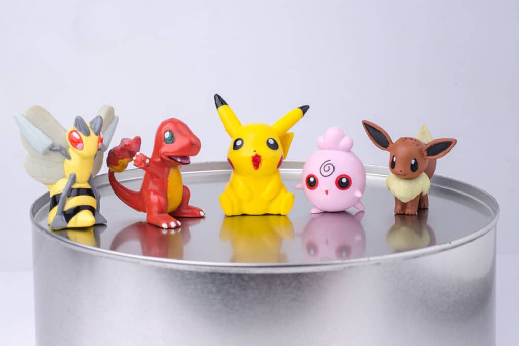 5 figurines pokemon alignée sur une boite en fer. Il y a un pokemon abeille, un salamèche, un pikachu, un evoli et un pokemon rose.