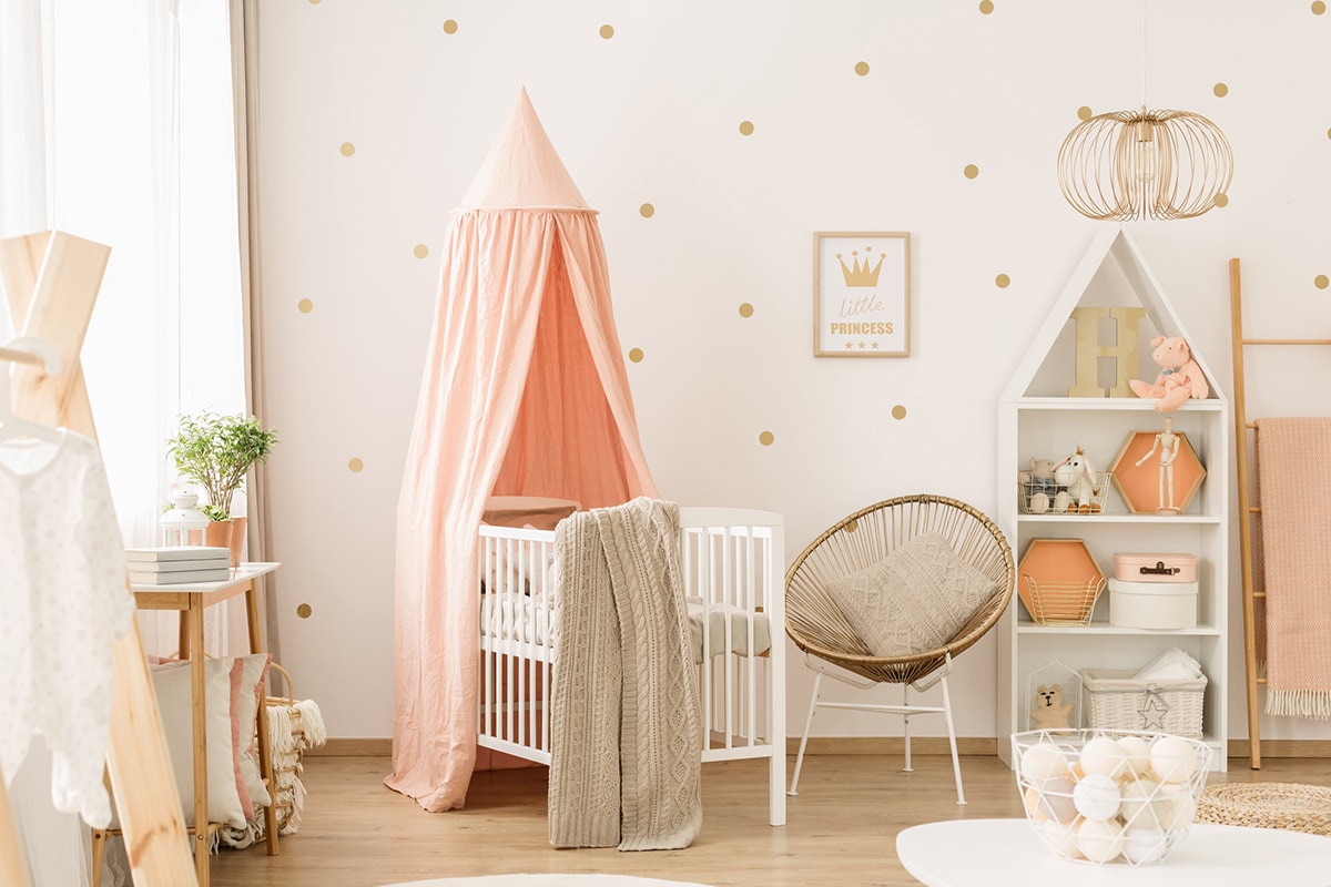 Une chambre pour enfant bien rangée. Les tons sont roses, il y a un lit pour bébé, des meubles de rangements et des décorations.
