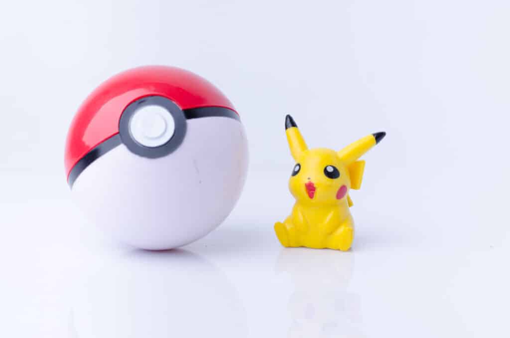 Un pokemon pikachu posé à coté d'une grande pokeball sur fond blanc