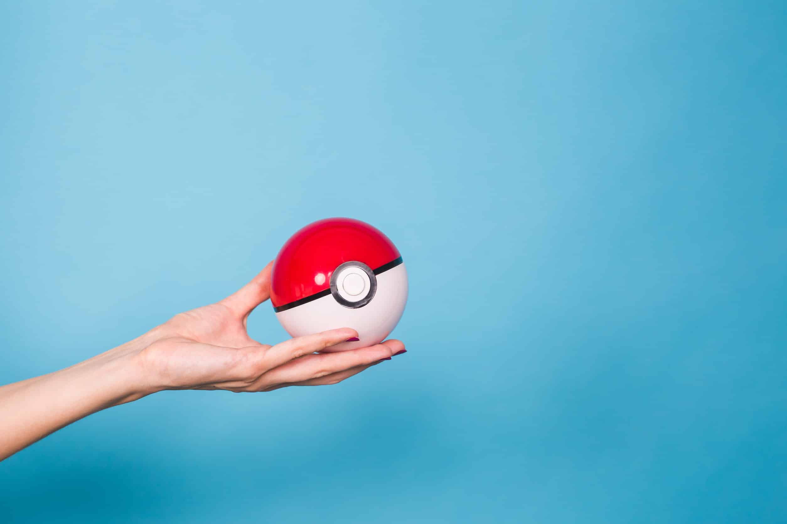 Une main tenant une pokeball de pokémon rouge et blanche sur fond bleu