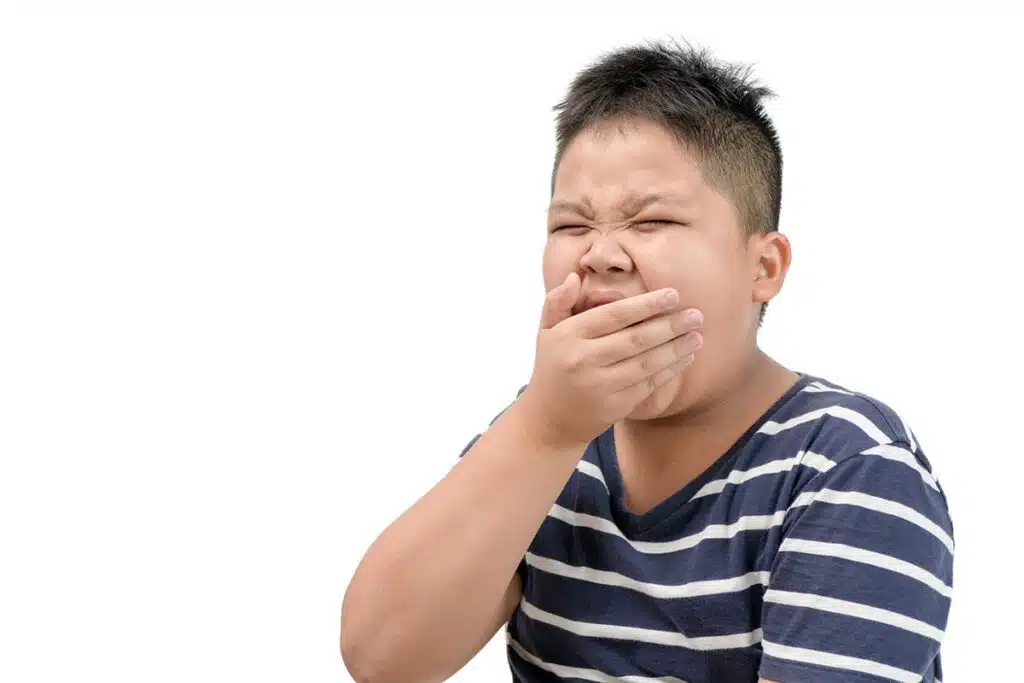 Un enfant qui baille avec sa main devant la bouche. Il porte un t shirt bleu à ligne blanches