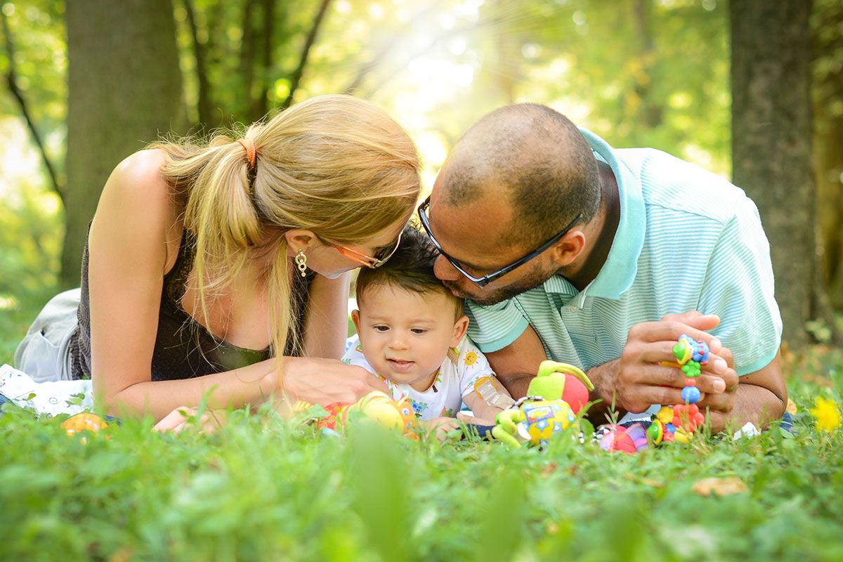 Une famille joyeuse couchée dans l'herbe. Il y a la maman, le papa et leur bébé au milieu.