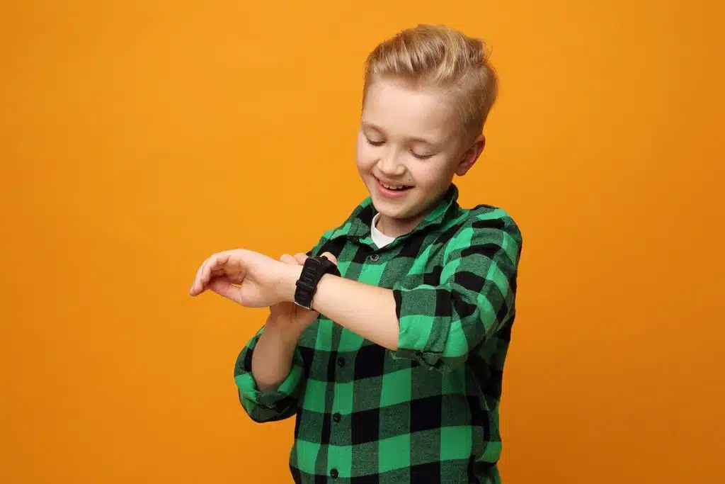 Un jeune garçon blond qui porte une chemise verte à carreaux et une montre enfant