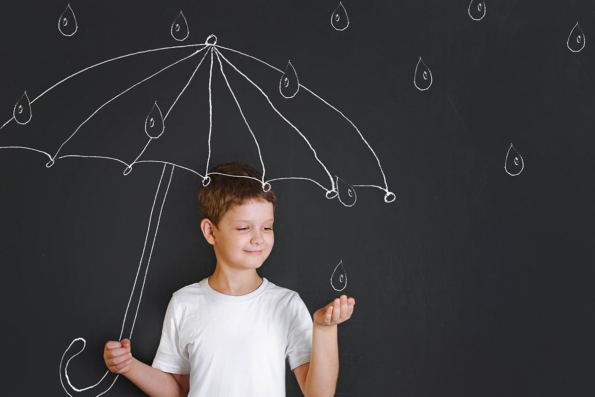 Un jeune garçon en t shirt blanc qui est devant un tableau ou il y a un parapluie pour enfant dessiné et des gouttes de pluies