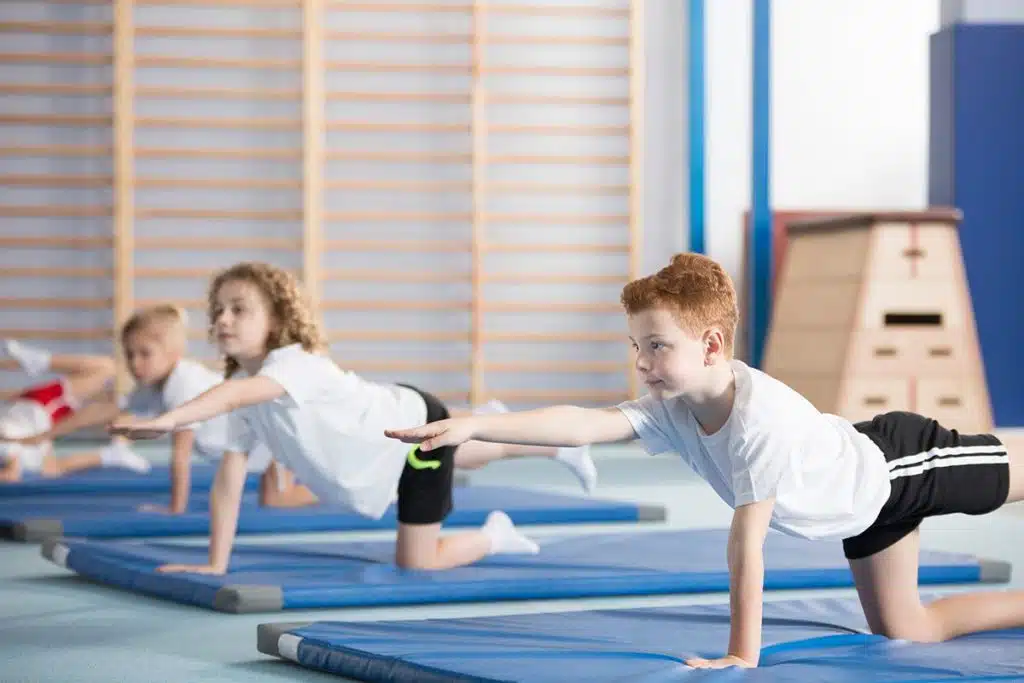 Un cours de gymnastique pour enfant. Il y a 4 enfants en tenues de sport sur des tapis de gym.