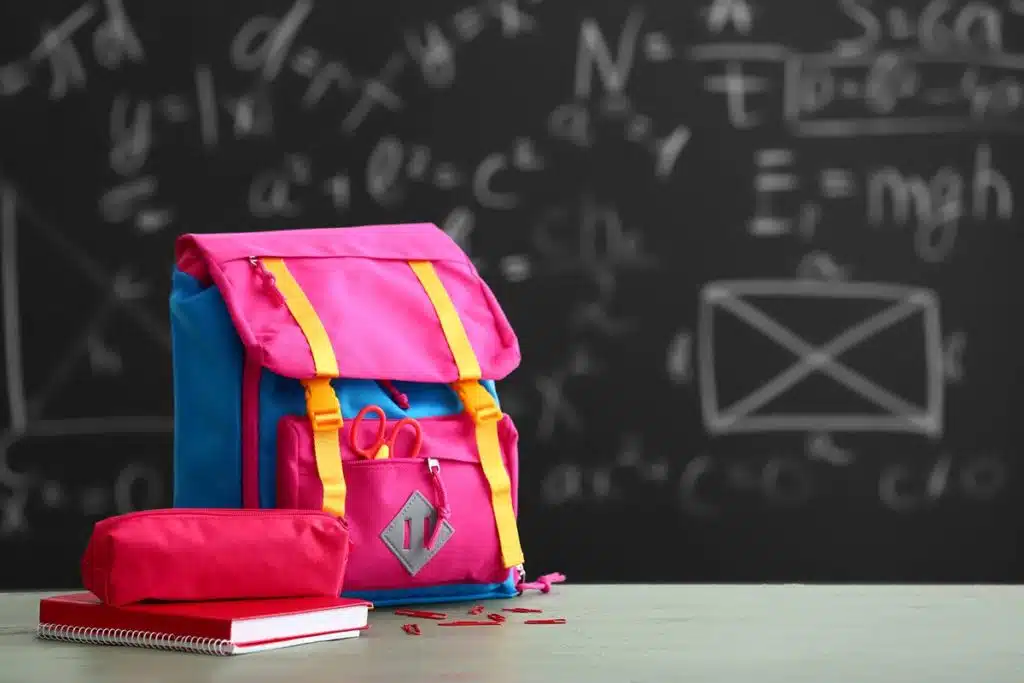 Un sac d'école pour enfant bleu et rose sur une table. Il y a un cahier d'école et une trousse