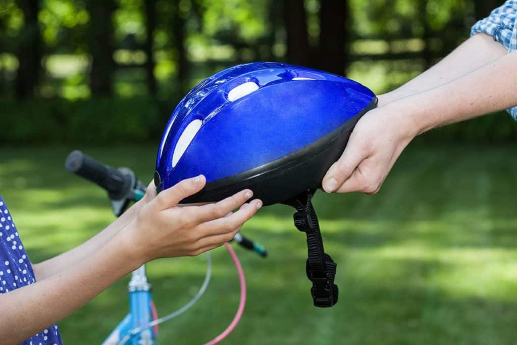 Une main qui tend un casque de vélo bleu à un enfant pour faire du vélo