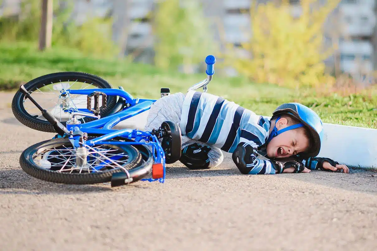 Un jeune enfant qui est tombé de son vélo bleu. Il pleure et porte un casque de vélo, des protèges genoux et des gants de protections noir