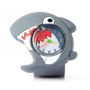 Une montre pour enfant en plastique représentant un requin mignon, au centre, elle a un cadran en verre avec à l'intérieur des aiguilles colorées, mais aussi les dents du requin imprimées.