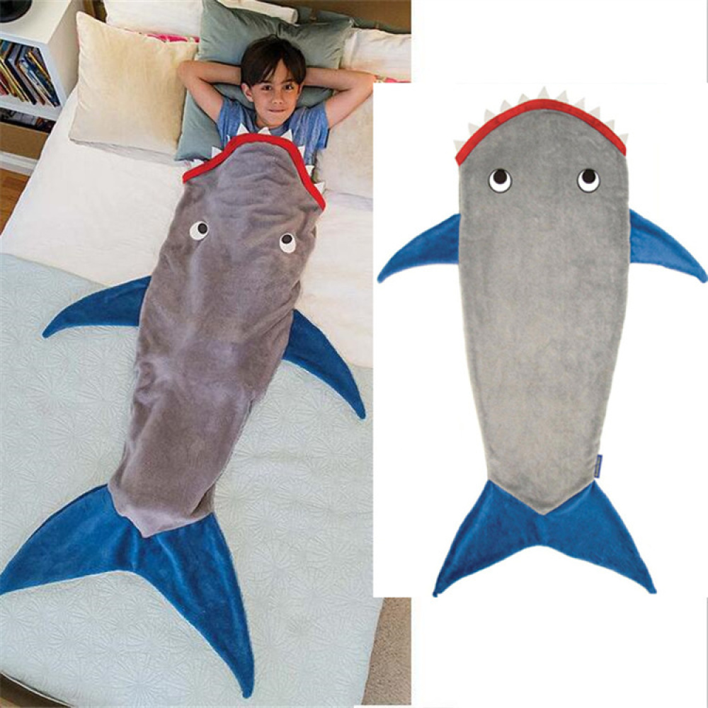 La photo est séparé en deux parties, la première représente un enfant coucher dans un lit, il est glissé dans un sac de couchage en forme de requin de couleur grise avec les nageoires bleues et la bouche rouge. La deuxième partie d'image représente ce sac de couchage sur un fond blanc.