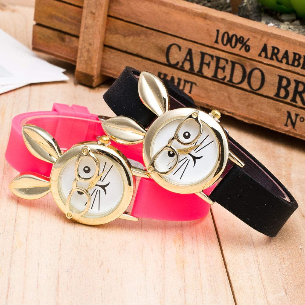 posées sur un table en bois, deux montres du même modèle , près d'un caisse en bois, une rose et une noir, leur cadrant est un petit lapin à lunettes mignon