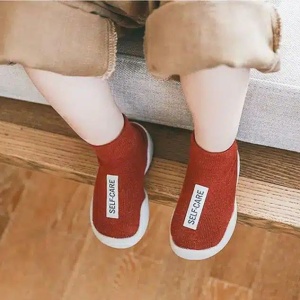 on voit des jambes d'un enfant assis portant des chausson-chaussettes rouge avec une étiquette blanche