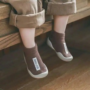 on voit des jambes d'un enfant assis portant des chausson-chaussettes marrons avec une étiquette blanche