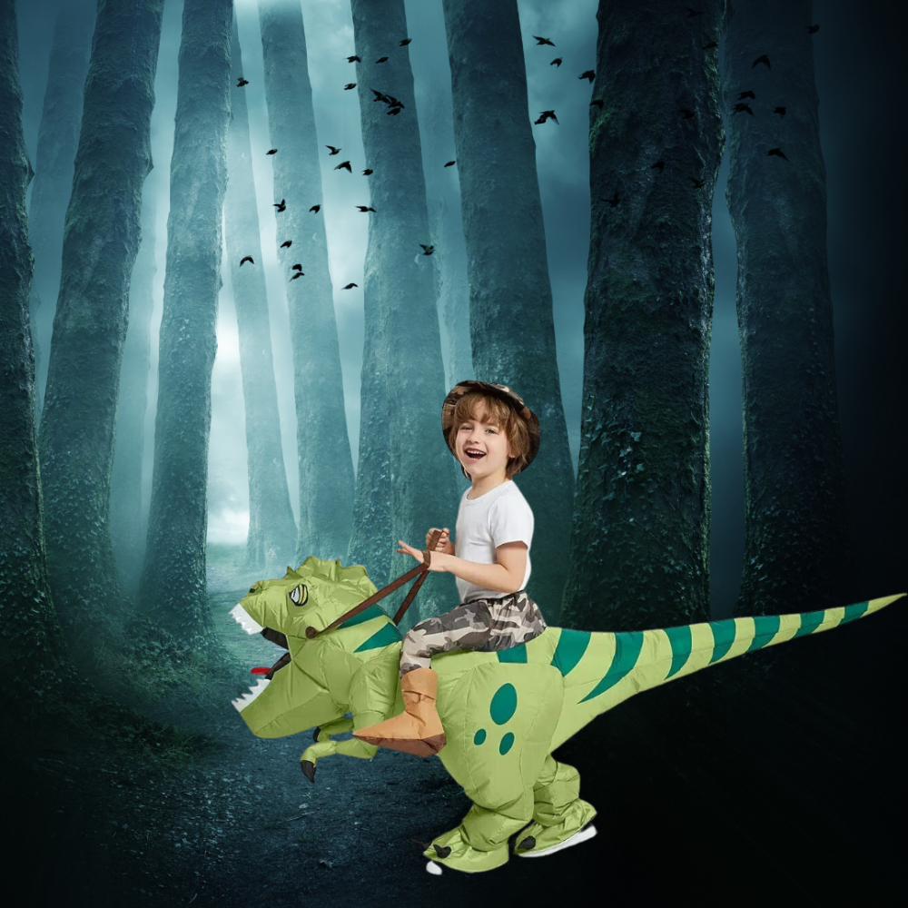 Jeune garçon souriant vêtu d'un costume de dinosaure gonflable vert, dans une forêt sombre avec des chauves-souris dans le ciel