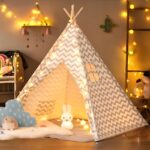 Tipi pour enfant avec une structure en bois et un tissu à motifs chevrons gris et blancs. L'intérieur est décoré avec des lumières douces et des coussins, créant un espace cosy et ludique, idéal pour jouer ou se détendre.