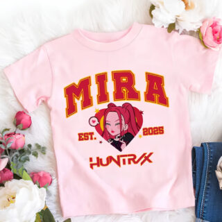 T-shirt enfant K-pop Demon Hunters rose Mira. Son prénom est écrit en majuscules rouge. En-dessous, le visage de Mira version cartoon. Encore en-dessous, Huntrix écrit en rouge. Le t-shirt est posé à côté de fleurs.