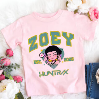 T-shirt enfant K-pop Demon Hunters rose Zoey. L'écriture de Zoey est en majuscules vertes. Au centre, le visage de Zoey. Le t-shirt est posé à côté de fleurs.