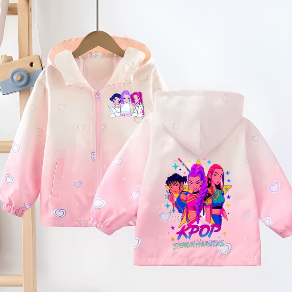 Veste enfant K-pop Demon Hunters coupe-vent imperméable. En premier plan, la veste vue de dos, de couleur rose et beige dégradés, à capuche avec un motif des 3 héroïnes du film dans le dos. Derrière, la veste vue de face, suspendue sur un cintre en bois, une fermeture éclair et un motif côté cœur. Sur la gauche, on aperçoit une échelle en bois.