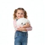 Jeune fille avec des couettes portant un jean et un t-shirt rose, se tient debout avec dans les bras un squishy dumpling blanc géant.